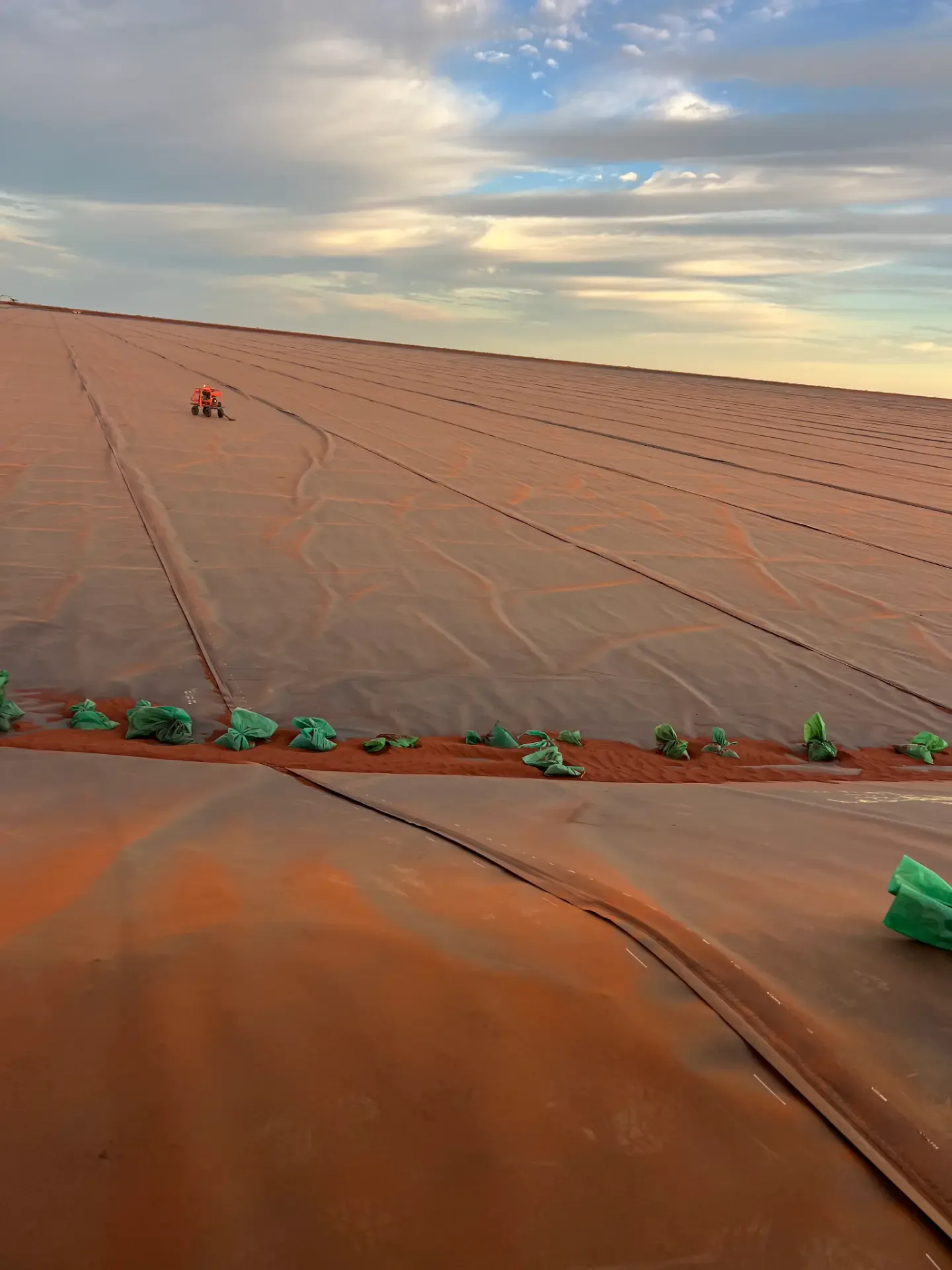 Large-scale geomembrane liner installation stretching to the horizon under a cloudy sky